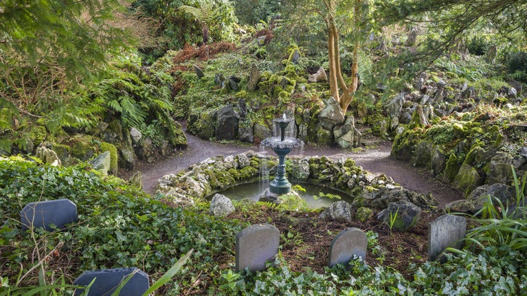 View of the Fernery, with abundant planting of a variety of ferns, paths lead around a central fountain and the graves of family dogs can be seen in the foreground